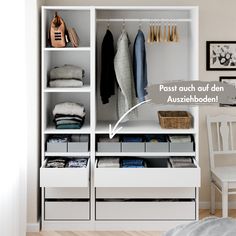 a white closet with drawers and clothes hanging on the wall, next to a chair