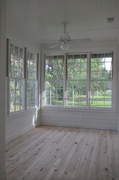 an empty room with white walls and wood flooring, windows open to the yard