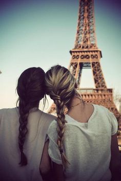 two girls standing in front of the eiffel tower with their backs to each other