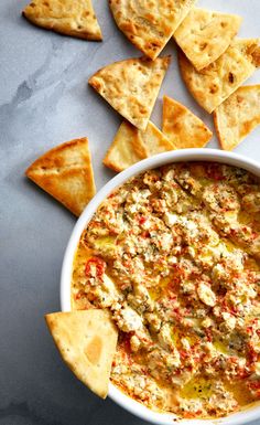 a white bowl filled with dip surrounded by tortilla chips on a gray surface