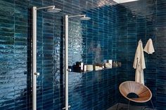 a blue tiled bathroom with a wooden chair and towel rack on the wall next to it