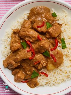 a white plate topped with rice and meat covered in gravy on top of a pink and white table cloth