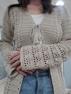 a woman is wearing a crocheted cardigan and has her hands in her pockets