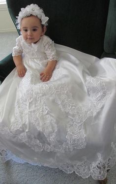 a baby in a white dress sitting on a green chair