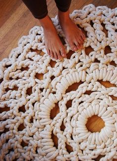 a person's feet on top of a crochet doily with wood flooring