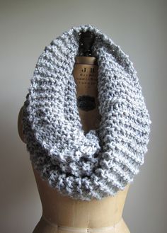 a gray and white knitted scarf sitting on top of a wooden mannequin