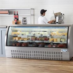 a man working behind the counter at a deli with cheeses and other foods