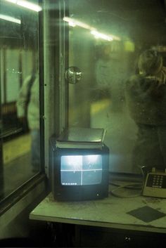 an old tv sitting on top of a table in front of a glass window with people standing around it