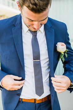 a man in a blue suit and tie is looking down at his pocket while holding a flower