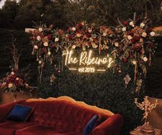 a red couch sitting in front of a lush green wall with flowers and greenery