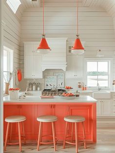 an orange island in a white kitchen with stools on the counter and two pendant lights hanging from the ceiling