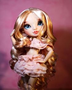 a close up of a doll with blonde hair and blue eyes wearing a pink dress