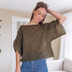 a woman standing in front of a white couch wearing a green sweater and blue jeans