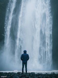 a man standing in front of a waterfall with his back to the camera looking at it