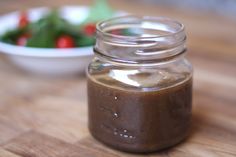 a glass jar filled with brown liquid sitting on top of a wooden table next to a bowl of salad