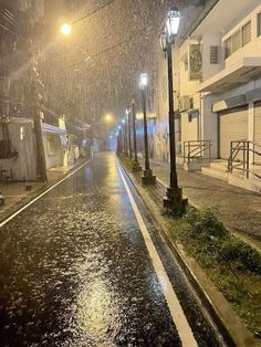 an empty city street at night with rain falling on the sidewalk and buildings in the background