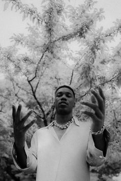 a black and white photo of a man holding his hands up in front of a tree