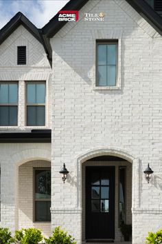 a large white brick house with two black doors and windows on either side of the front door