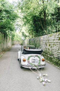 an old white car parked on the side of a road next to a brick wall