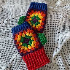 two colorful crocheted mittens sitting on top of a white tablecloth covered surface