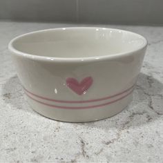 a white bowl with a pink heart painted on the side sitting on a marble counter