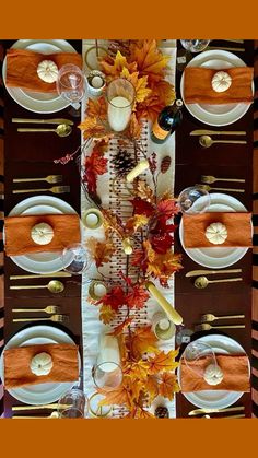 the table is set with white plates, silverware and autumn leaves on it's placemats