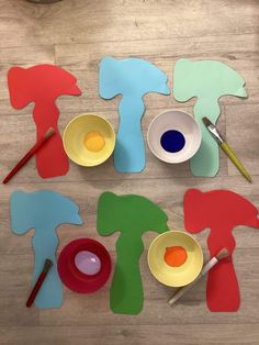 paper cutouts with paints and paintbrushes on a wooden floor next to bowls