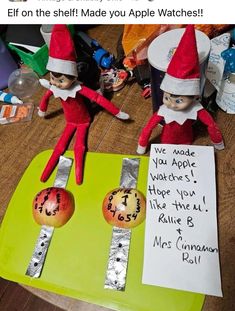 two elfs are sitting on top of a table with an apple and another sign