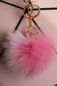 a pink pom - pom keychain hanging from a white handbag