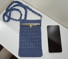 a crocheted blue purse sitting next to a cell phone on a white table