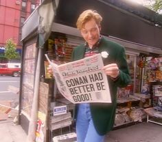 a man reading a newspaper while standing on the side of a street in front of a store