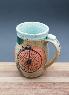 a ceramic mug with a bicycle painted on the front and side, sitting on a wooden surface