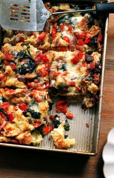 a pan filled with pizza sitting on top of a wooden table next to a spatula