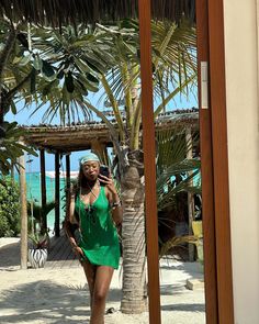 a woman in a green dress standing next to a palm tree and looking at her cell phone