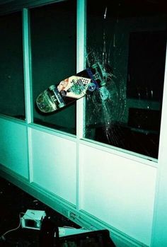 a broken window with a skateboard stuck in it and the glass is cracked off