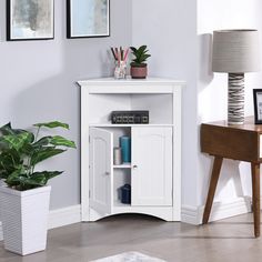 a white corner cabinet next to a potted plant