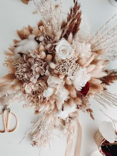 an arrangement of dried flowers, feathers and scissors on a white table with other items