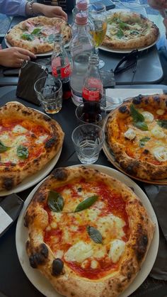 three pizzas on plates sitting on a table next to bottles of water and glasses