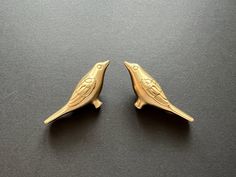 two small gold birds sitting next to each other on a black counter top in front of a gray background