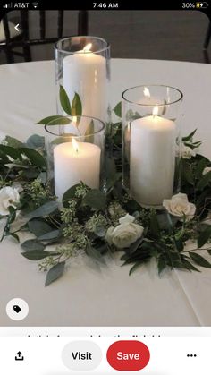 a table topped with candles and flowers on top of a white table cloth covered in greenery