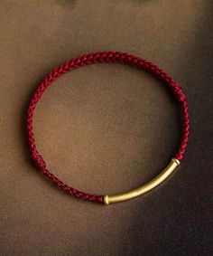 a red rope bracelet with a gold bar on the end, sitting on a table