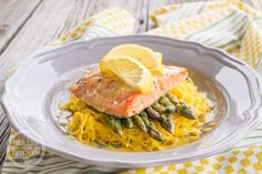 a white plate topped with salmon and asparagus on top of yellow noodles next to a lemon wedge