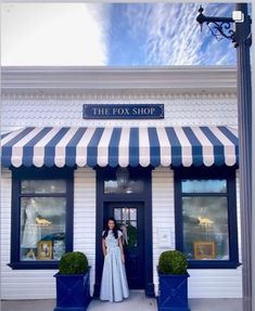 a woman standing in front of a store with blue and white striped awnings