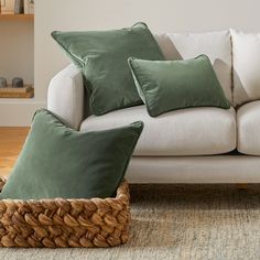 a white couch with green pillows and a basket on the floor in front of it