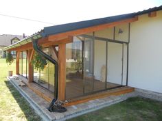 a small house with glass walls and wood trimmings on the roof, sitting in front of a grassy yard