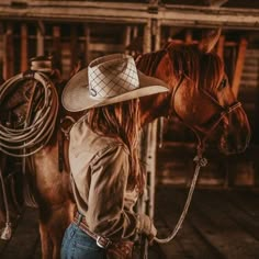 a woman wearing a cowboy hat standing next to a horse