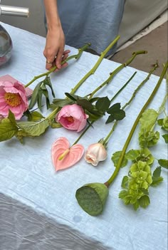 someone is arranging flowers on a table with white linens and blue cloth, including pink roses