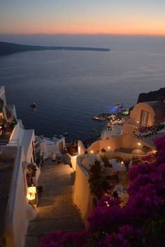 an outdoor restaurant overlooking the ocean at dusk with people sitting on steps leading to it