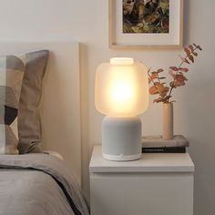 an amazon echo sitting on top of a nightstand next to a bed with a plant