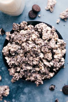 a bowl filled with cookies and oreo chips next to a glass of milk on a blue surface